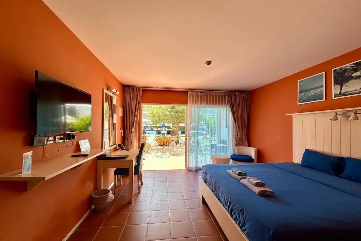 Quarto de hotel com cama, escrivaninha com cadeira, televisão e vista para a área externa.