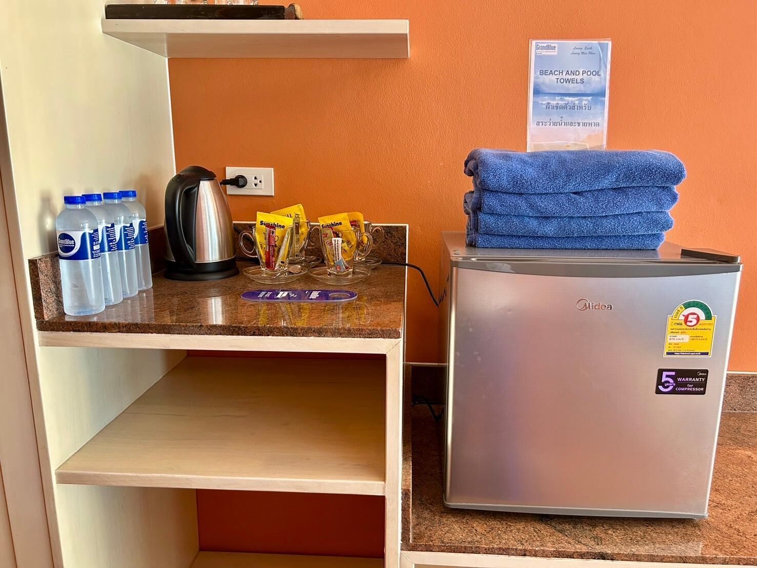 A kitchenette with a coffee maker, bottled water, tea packets, and a refrigerator.