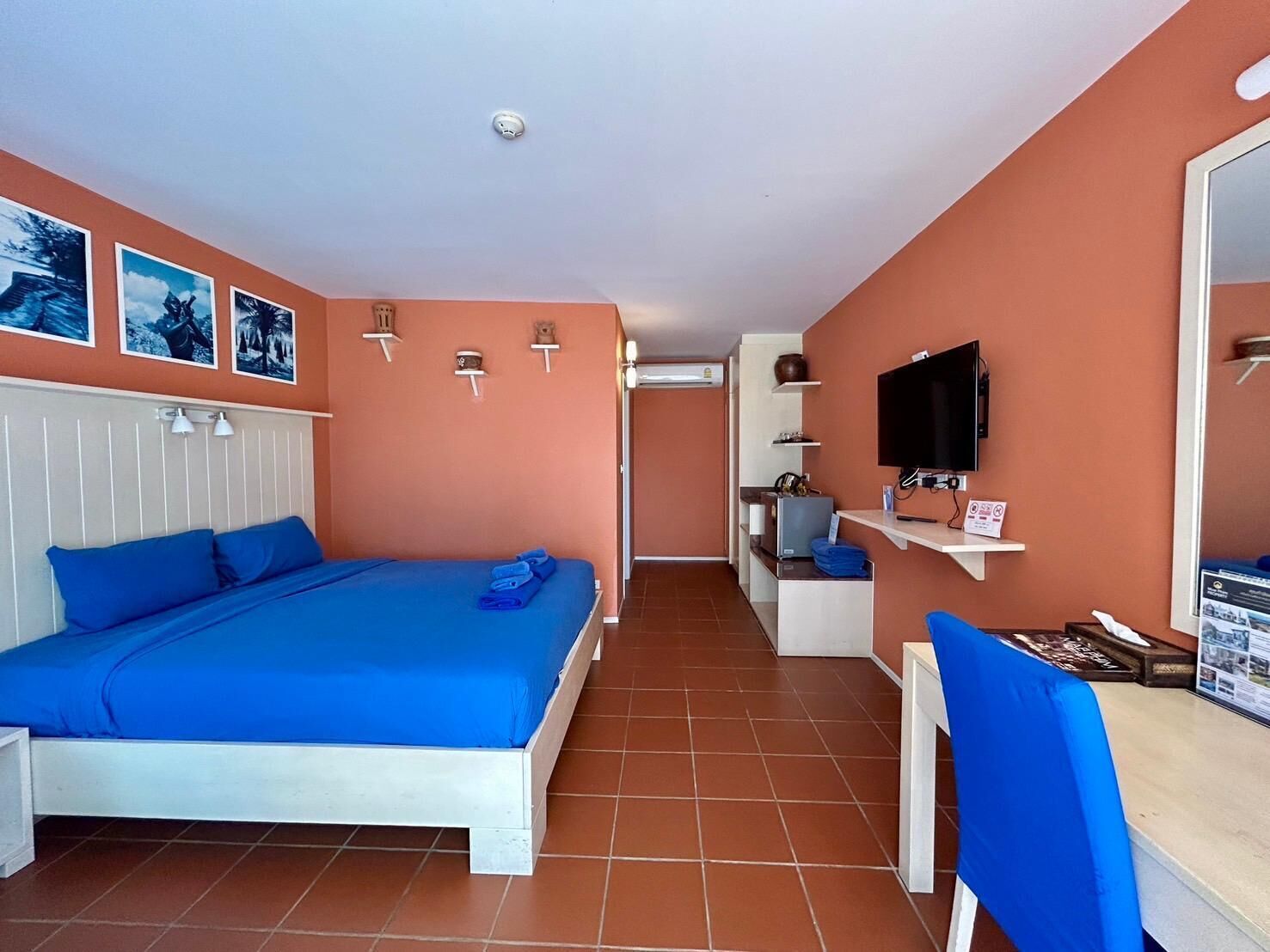 A bedroom with a bed, a desk, a chair, a TV, and a shelf with items.