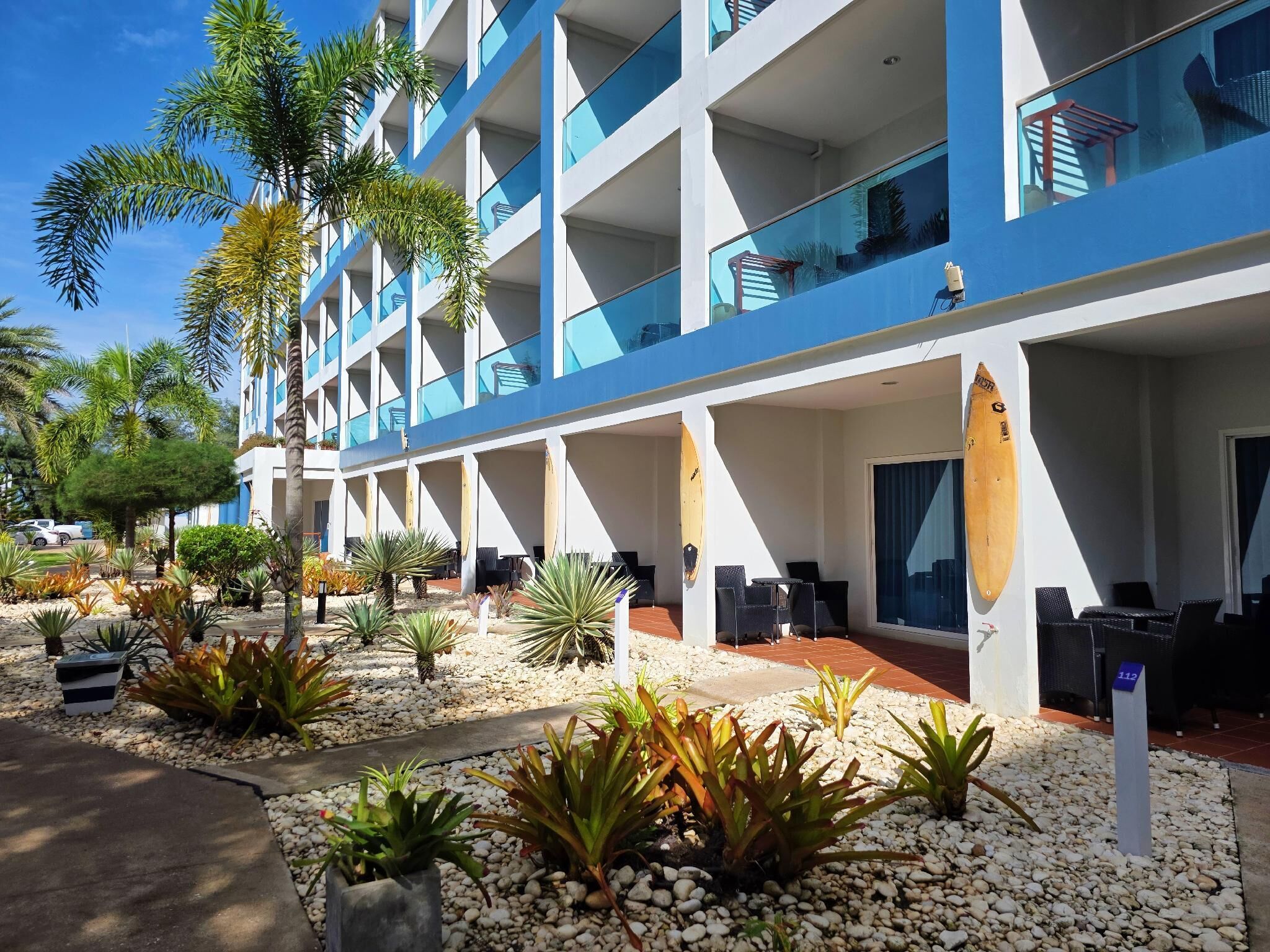 A modern hotel with multiple balconies, outdoor seating areas, and a variety of tropical plants.
