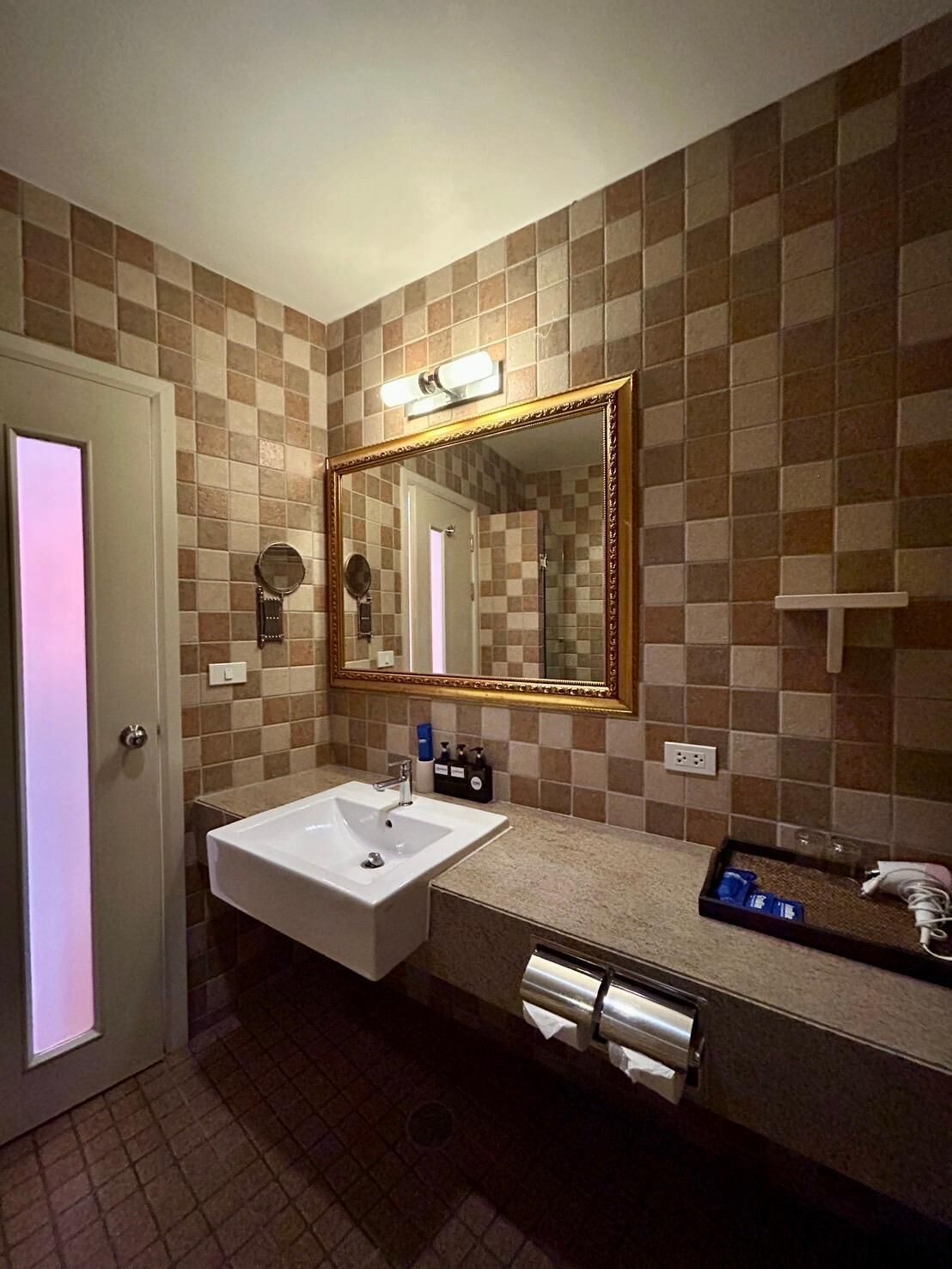 Un baño con un lavamanos blanco, un espejo grande y una pared con azulejos.