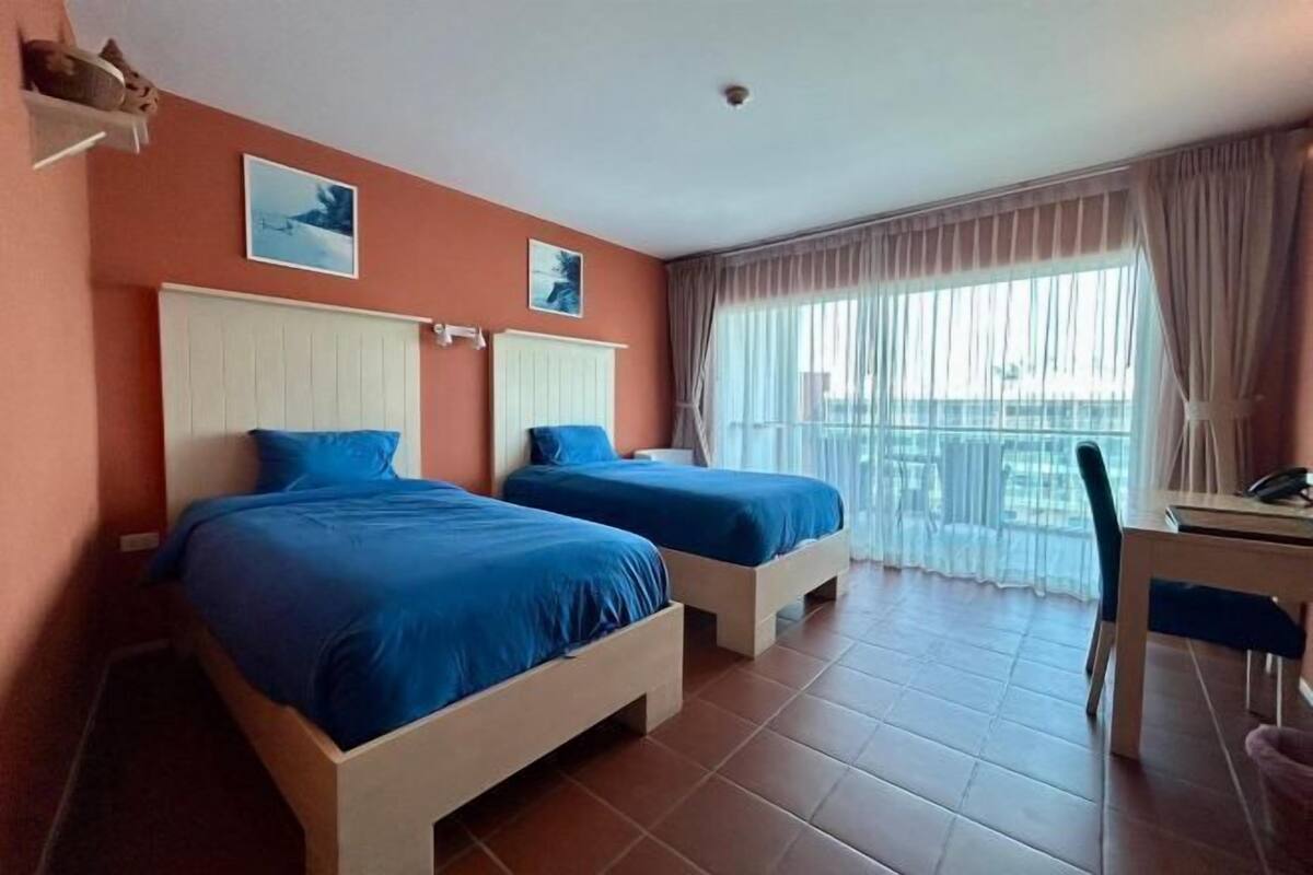 Quarto de hotel com duas camas, uma escrivaninha e uma cadeira.