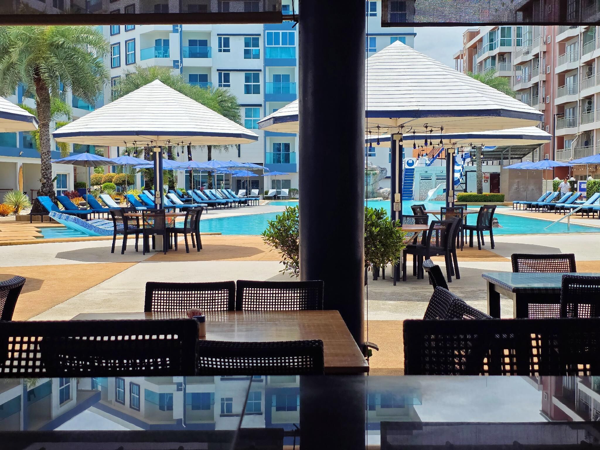 A poolside area with lounge chairs and umbrellas, a pool, and a view of multi-story buildings.