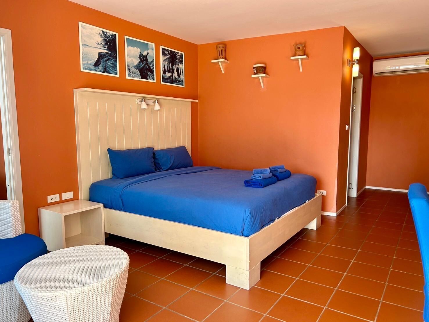 Un dormitorio con cama, mesita de noche, una silla y estante de pared con objetos decorativos.