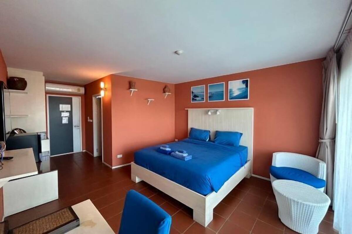 Quarto de hotel com cama, uma cadeira, escrivaninha e mesa pequena.