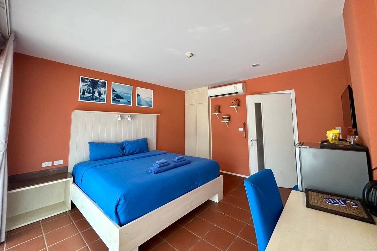 Quarto com cama, escrivaninha e cadeira. Três quadros pendem na parede acima da cama.