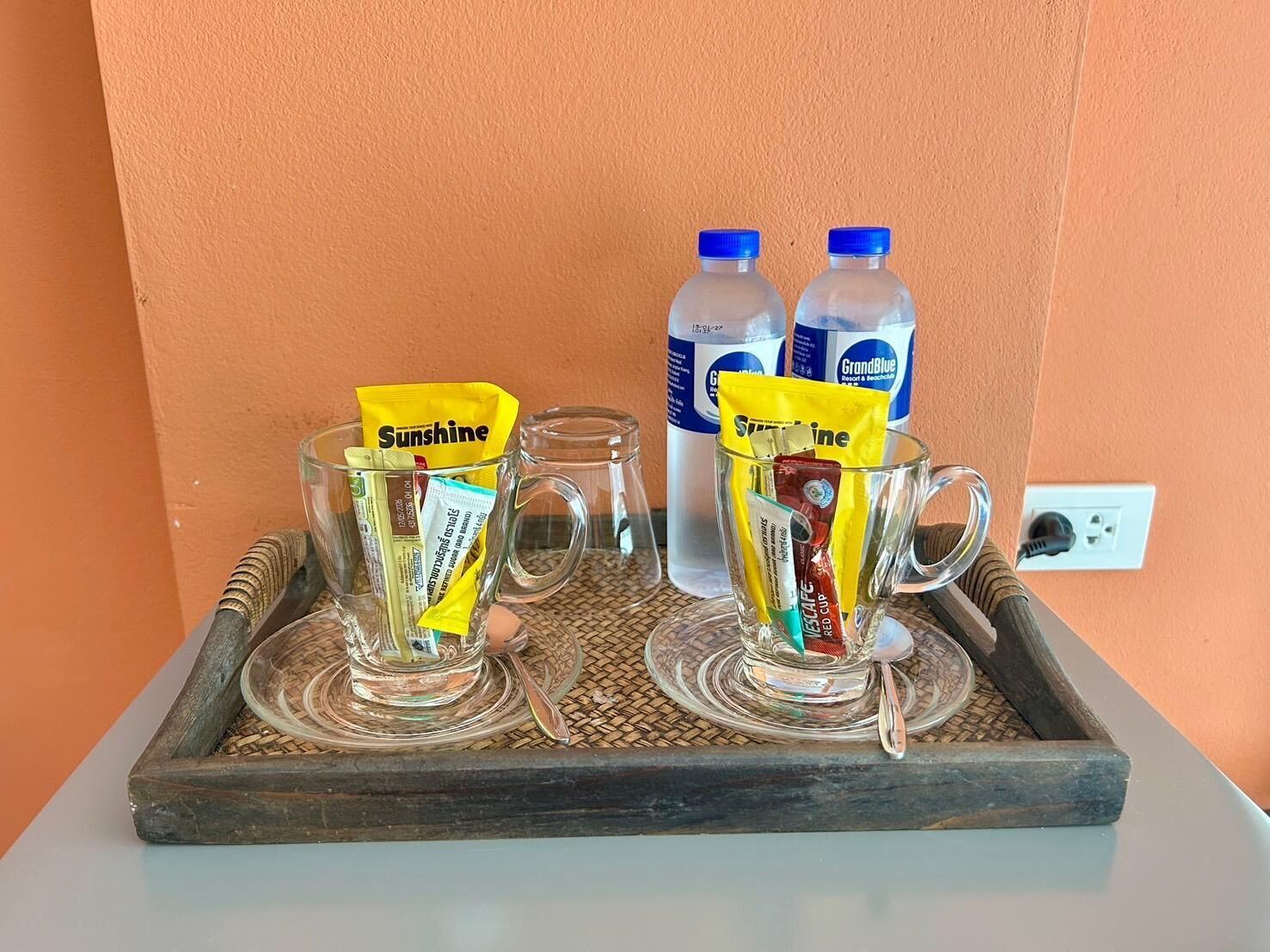 Two clear glass mugs on a tray with packets of Sunrise coffee and a bottle of GrandBlue water.