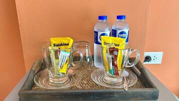 Two clear glass mugs on a tray with packets of Sunrise coffee and a bottle of GrandBlue water.