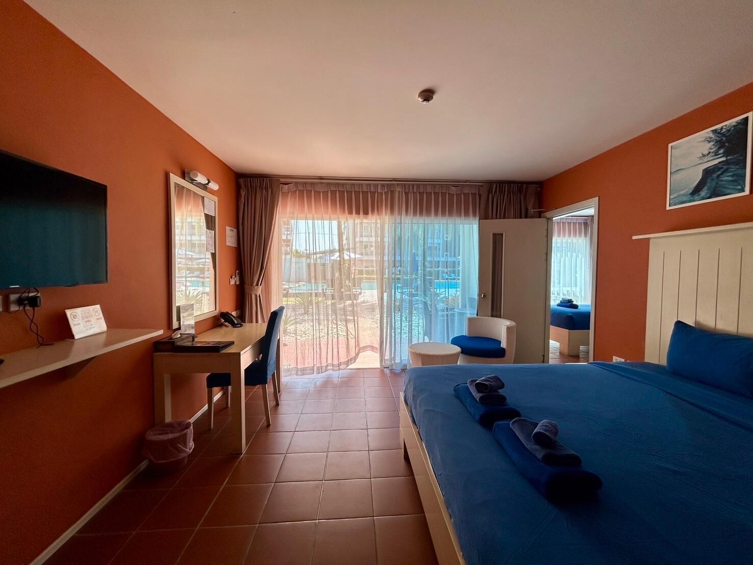 A hotel room with a bed, desk, chair, and a view of the outdoor area.