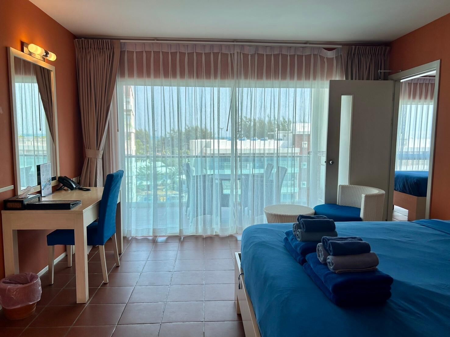 A hotel room with a bed, a desk, a chair, a small table, and a balcony with a view.