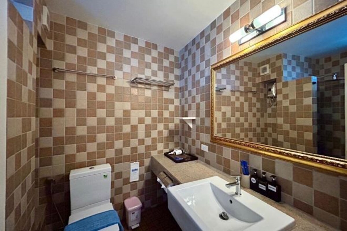 Une salle de bain avec des murs carrelés à motifs à carreaux, un lavabo blanc, un miroir avec un cadre doré et un porte-serviettes.