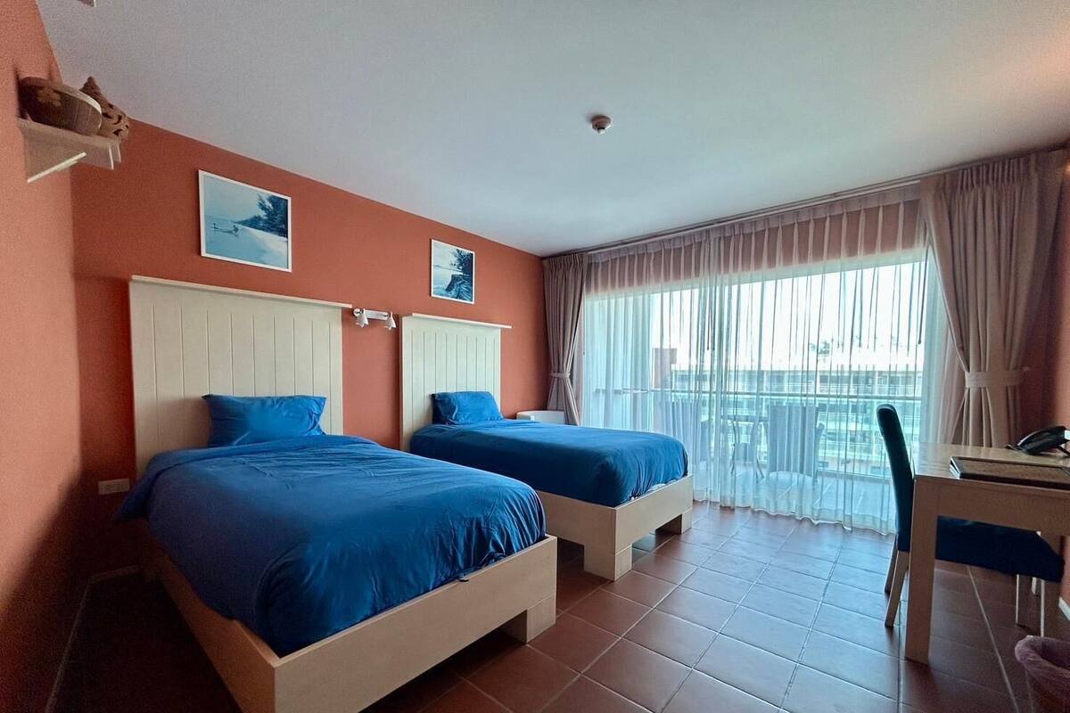 Quarto de hotel com duas camas, uma escrivaninha e varanda com vista.