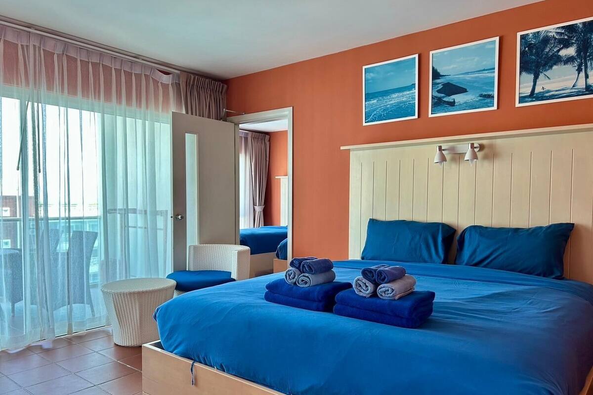 Quarto de hotel com uma cama grande, duas almofadas, uma cadeira e vista para o oceano pela janela.