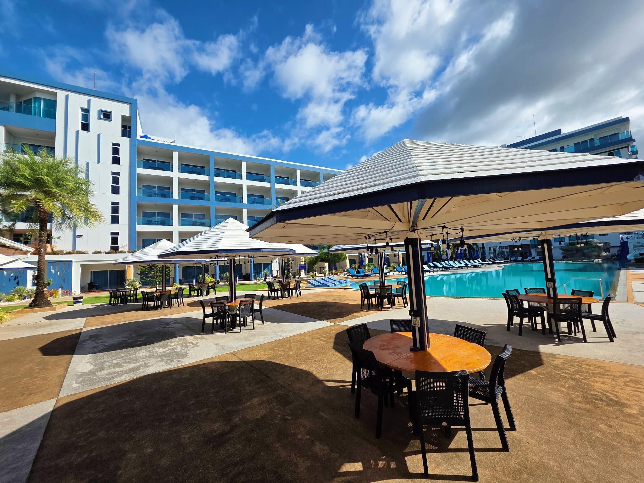 Un resort con zonas de estar al aire libre, piscina y un edificio moderno al fondo.