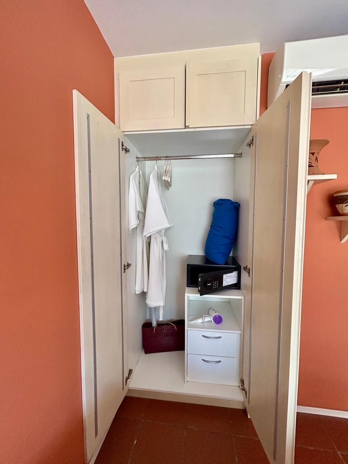 Un dressing avec des vêtements suspendus, un sac bleu, un sèche-cheveux et une petite étagère.
