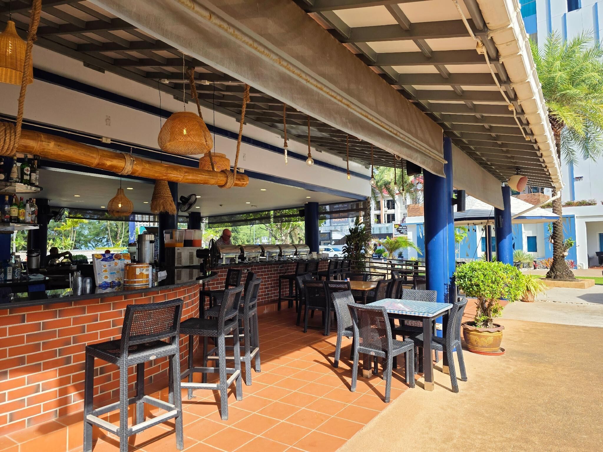 An outdoor cafe with a brick counter, wicker chairs, and hanging lights.