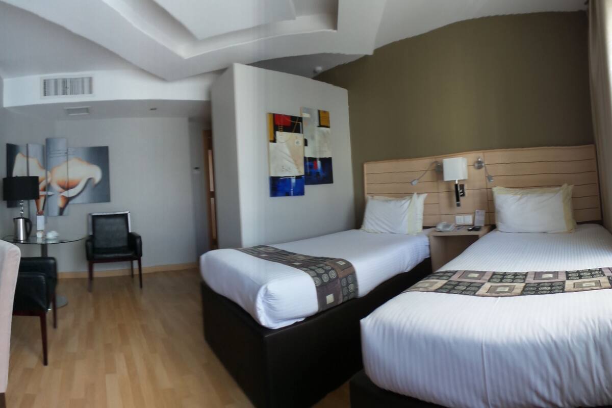 A hotel room with two beds, a desk, a chair, and a small table.