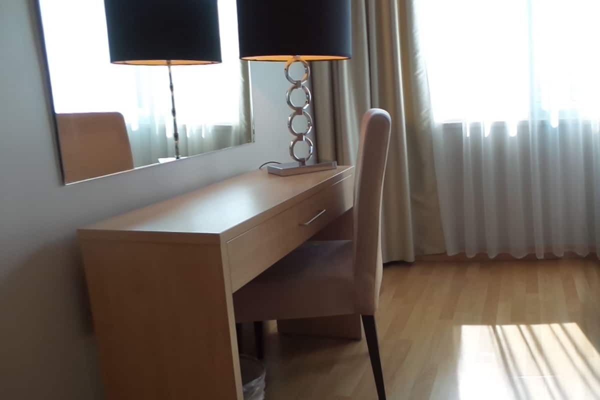 A hotel room with a bed, a desk, a chair, a lamp, and a window with curtains.