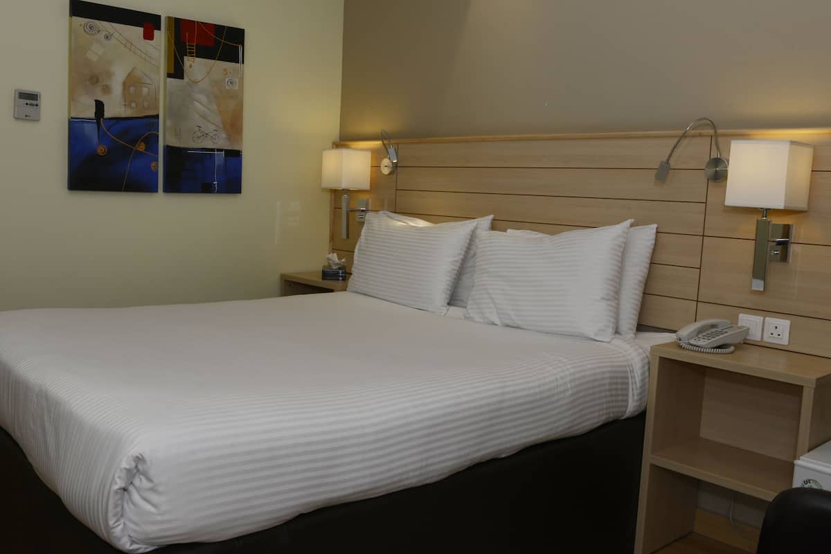 A hotel room with a large bed, two bedside tables, a lamp, and a phone on the nightstand.