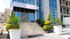 A modern hotel entrance with a glass facade, a staircase leading to the entrance, and potted plants. - Crystal Hotel (Amman)
