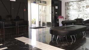 A lobby with a reception desk, black leather seating, a marble floor, and a large wall mural. - Crystal Hotel (Amman)