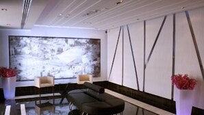 A modern lobby with a black leather sofa, two wooden chairs, a large abstract painting, and a glass floor. - Crystal Hotel (Amman)