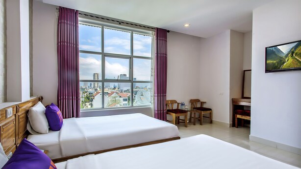 Una habitación de hotel con dos camas, un escritorio, sillas y un amplio ventanal con vistas a la ciudad.