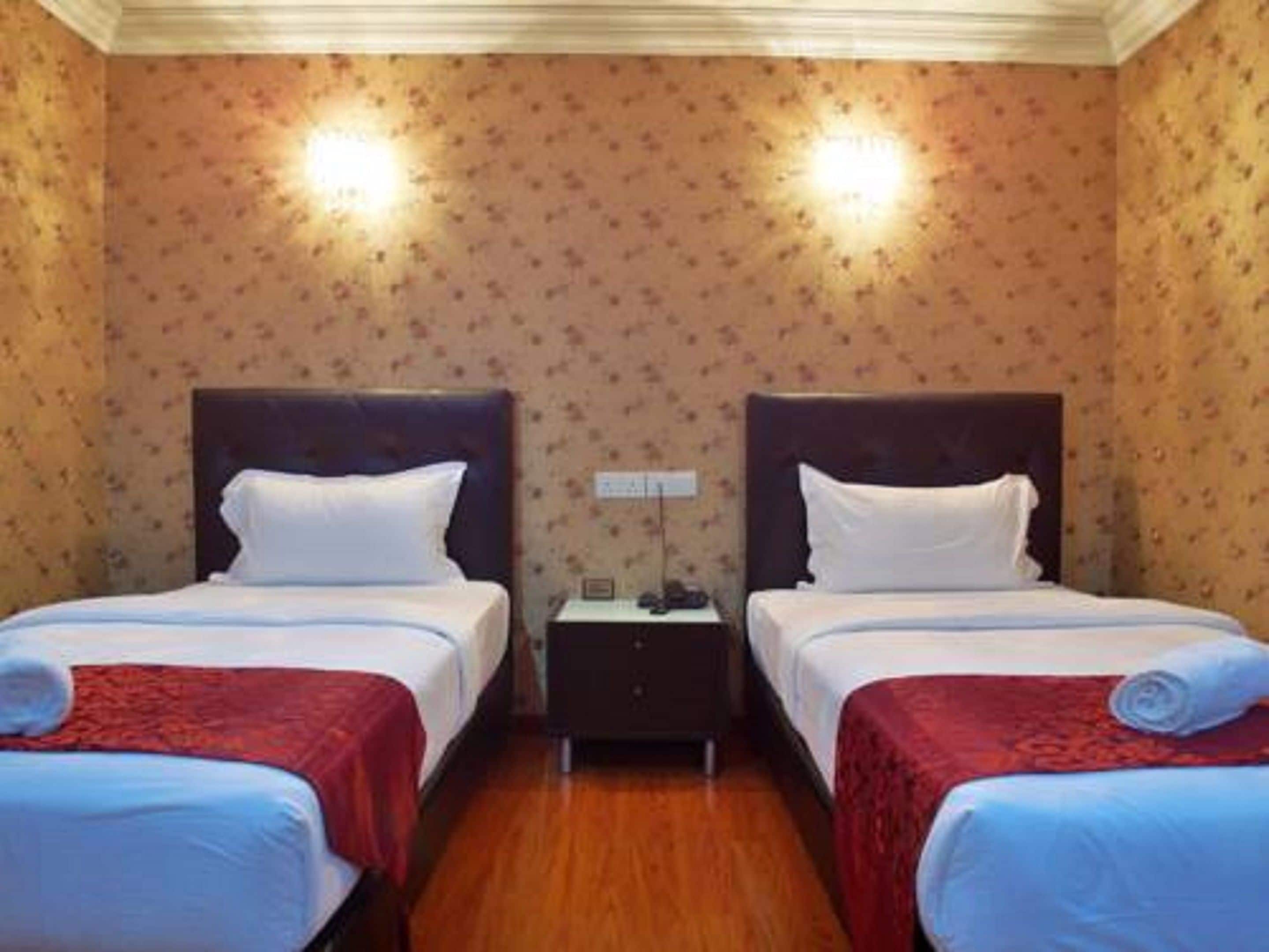 A hotel room with two beds, wooden flooring, and floral wallpaper.