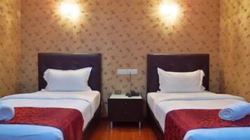 A hotel room with two beds, wooden flooring, and floral wallpaper.