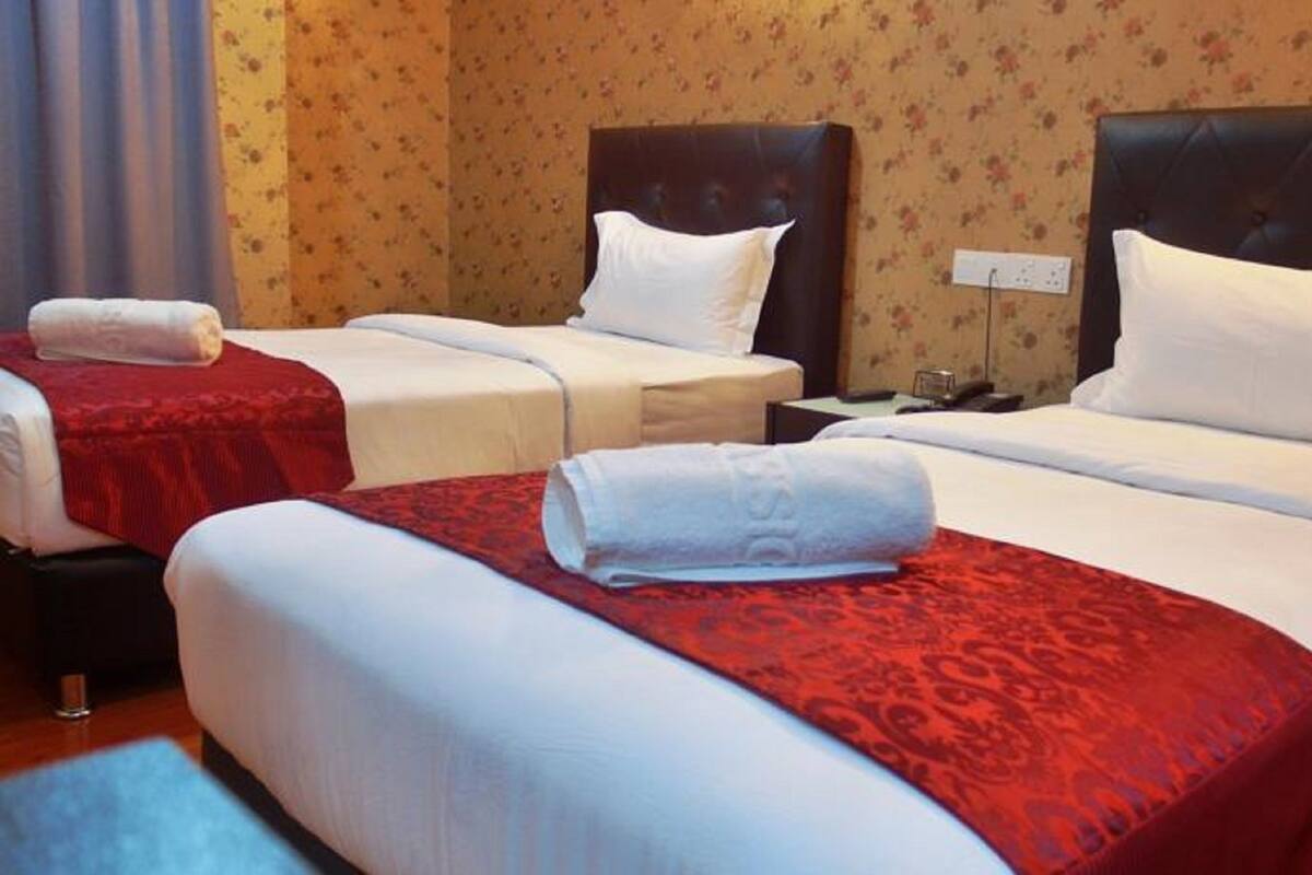 Habitación de hotel con dos camas, cada una con cubrecama rojo y ropa de cama blanca. Hay una mesita de noche con una lámpara y una pequeña mesa entre las camas.