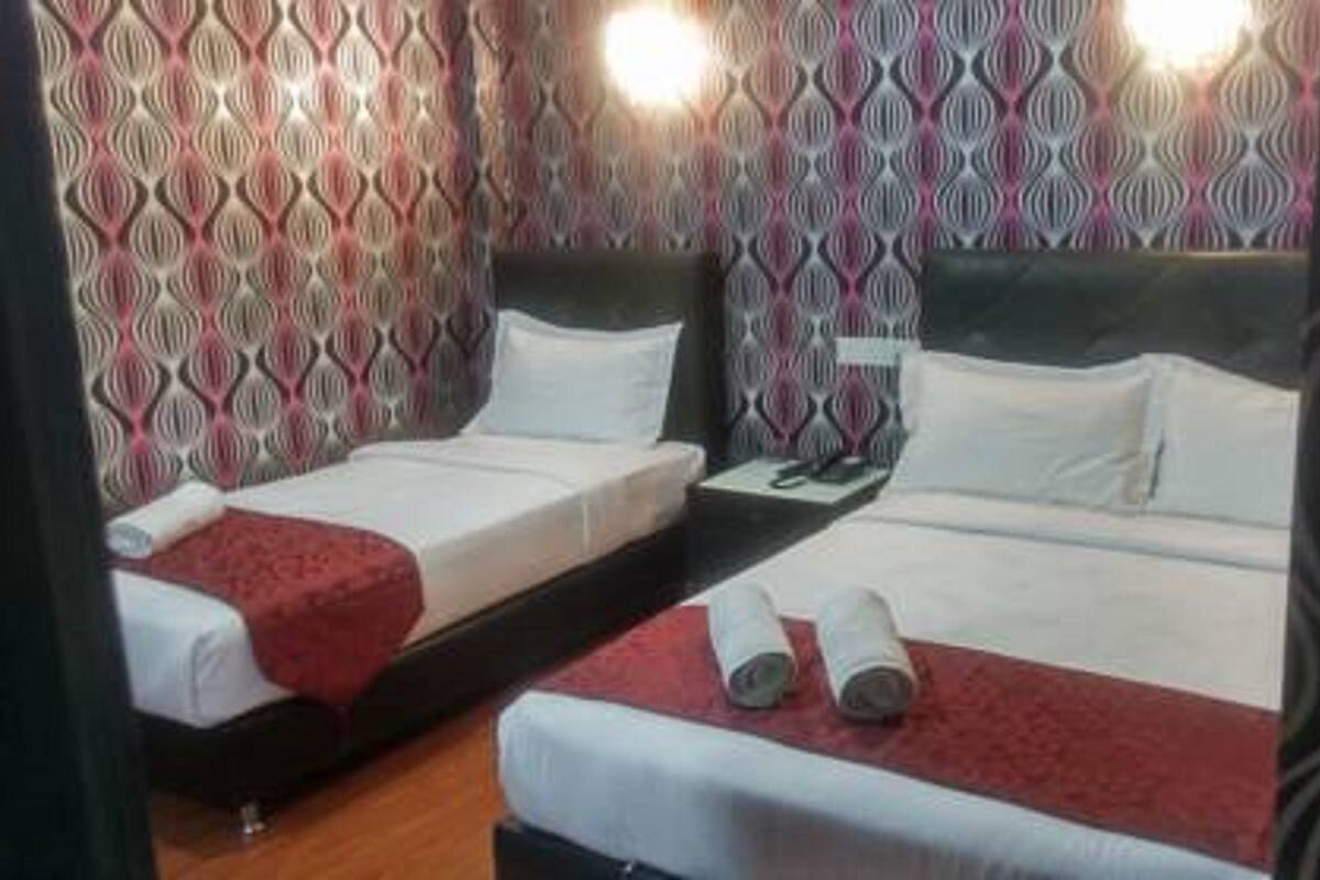 Habitación de hotel con dos camas, cada una con ropa blanca y mantas rojas. Hay dos mesitas de noche con lámparas y una mesita pequeña con un teléfono. Las paredes tienen un papel tapiz estampado.