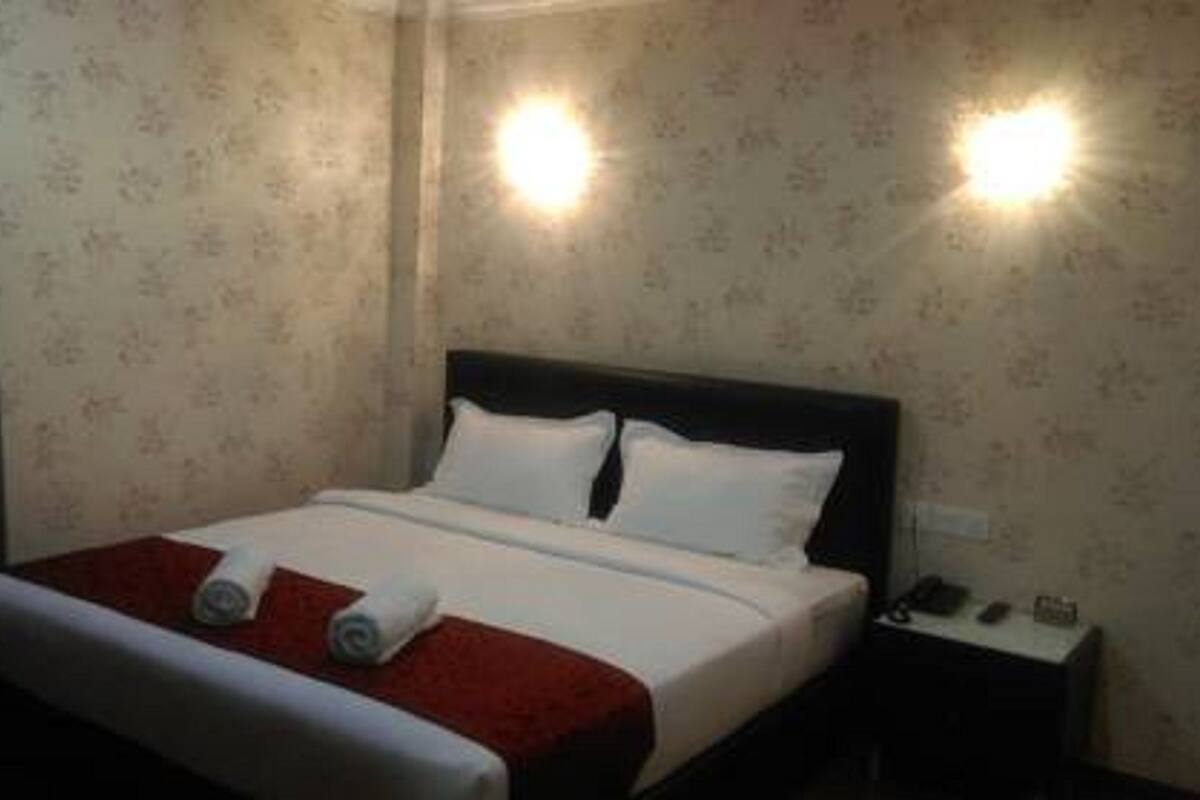Habitación de hotel con cama, dos almohadas, colcha roja y blanca, y dos luces fijadas a la pared.