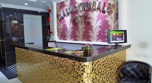 Un comptoir d’accueil d’hôtel orné d’un motif en mosaïque dorée, doté d’un écran numérique et d’une enseigne indiquant « CLASSIC KINABALU HOTEL ».