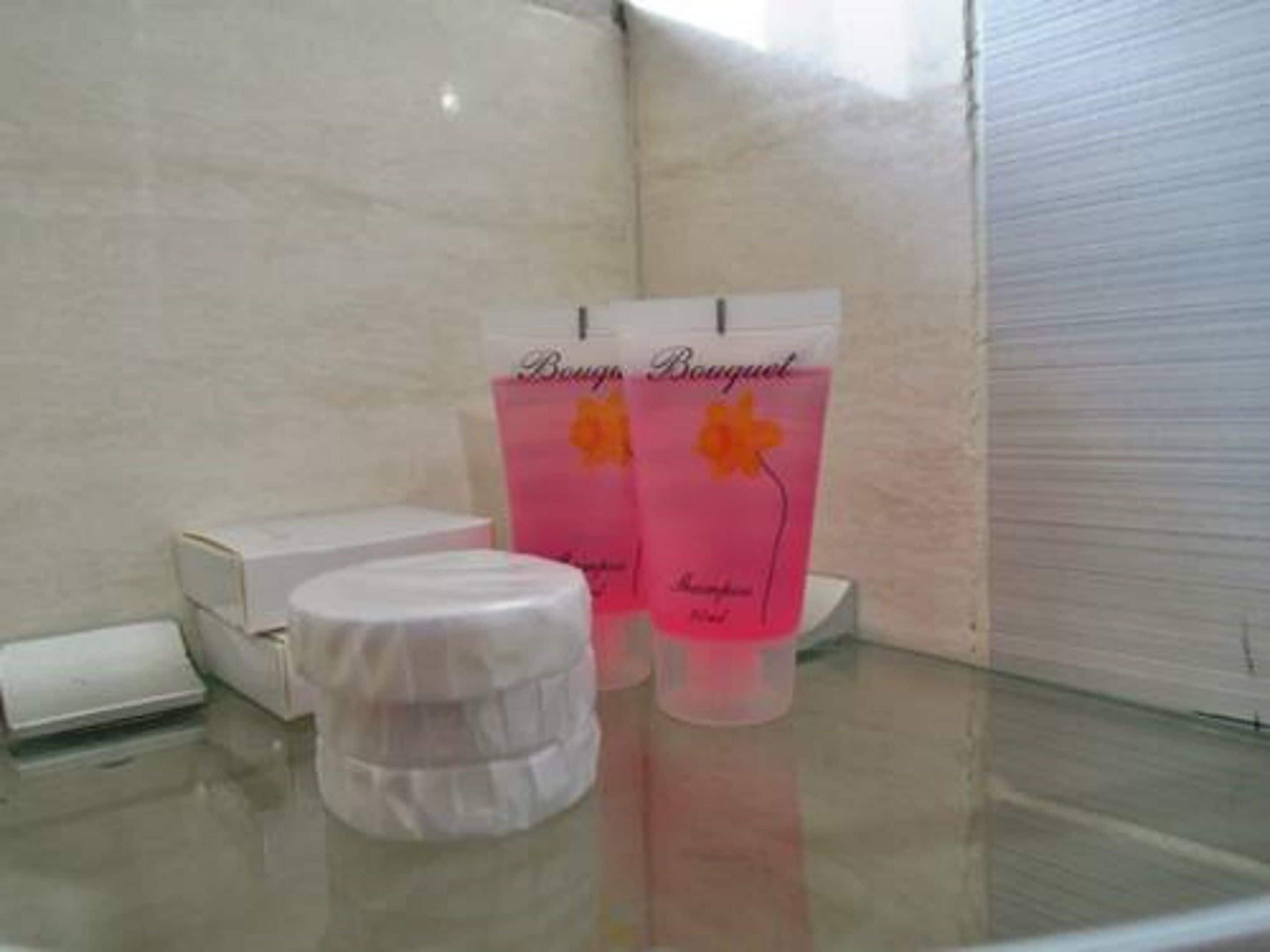 A bathroom with a glass shower enclosure, a white toilet, and a pink bottle of shampoo on the counter.