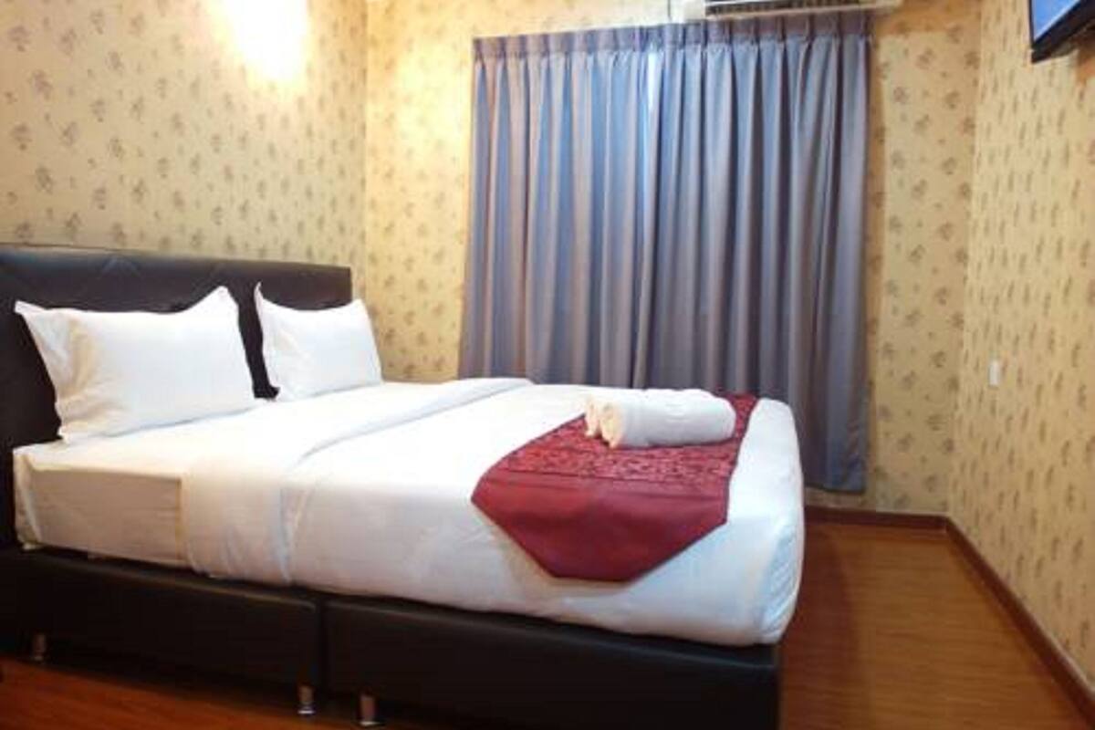 Una cama bien hecha con sábanas blancas y una manta roja, cabecera oscura y suelo de madera.