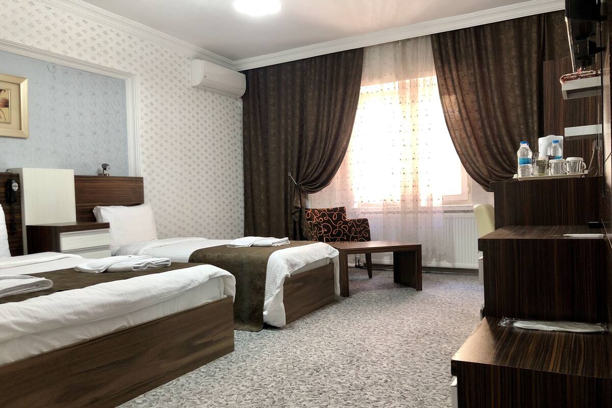 A hotel room with two beds, a desk, a chair, and a window with curtains.