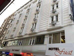 A hotel facade with multiple air conditioning units, a sign for 'HOTEL Fuat', and a storefront with 'IPHONE E MOBILE' signage. - Hotel Fuat (Van)