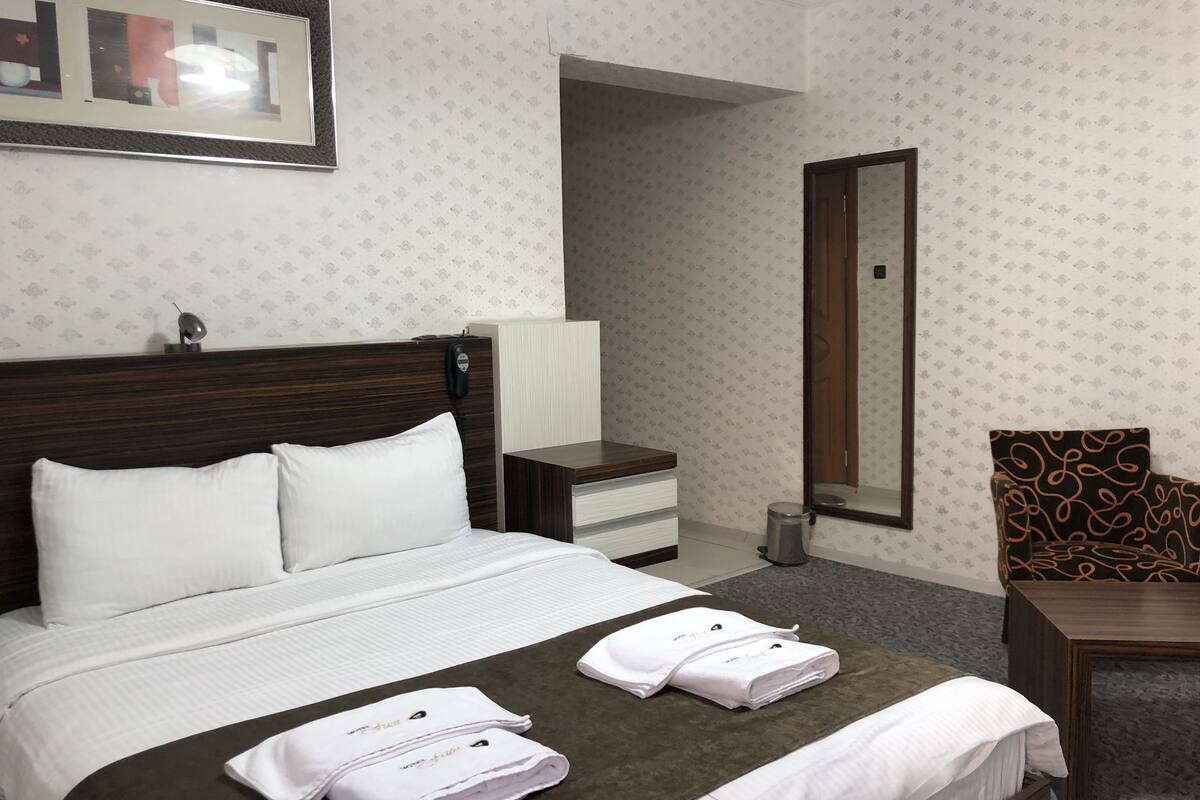 A hotel room with a bed, a nightstand, a chair, and a mirror.