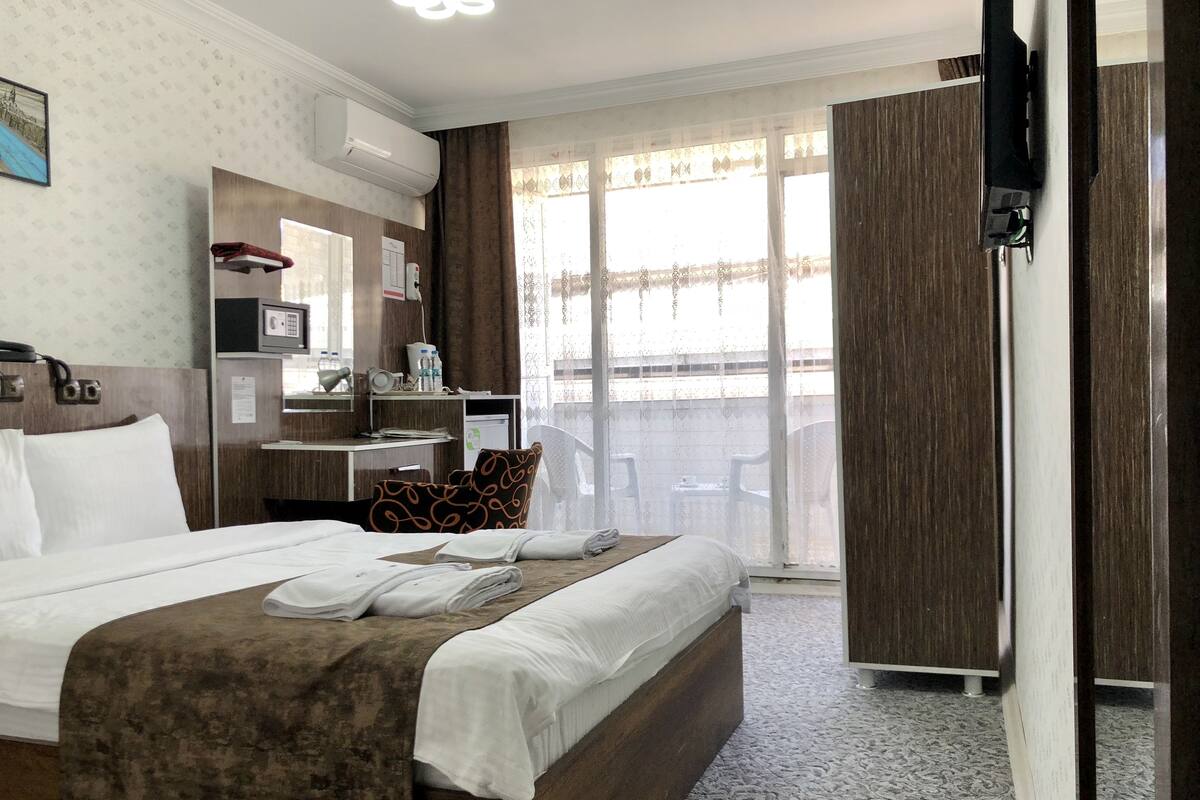 A hotel room with a bed, a desk, a chair, a minibar, and a balcony with a view.