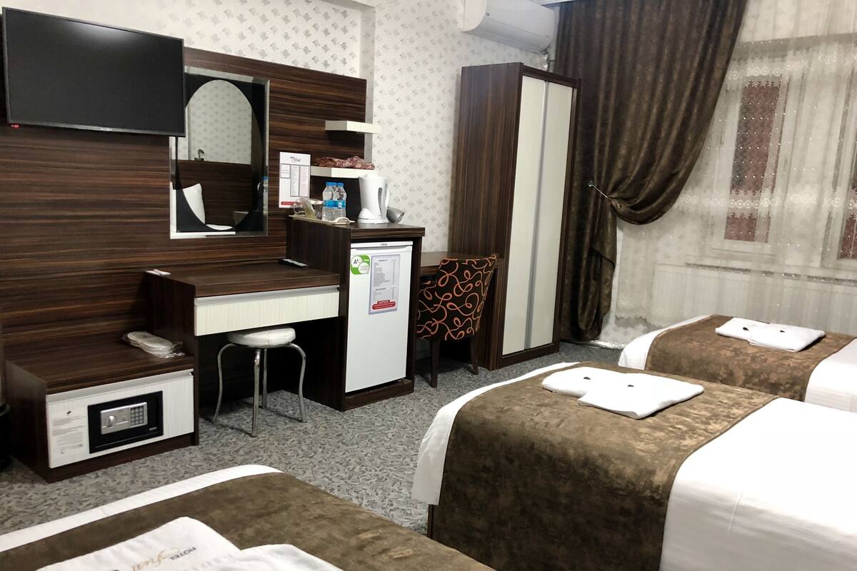 A hotel room with two beds, a desk, a chair, a minibar, a mirror, and a wardrobe.