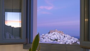 Vista de un pueblo costero desde una ventana, con una planta en maceta y un libro abierto sobre una mesa.