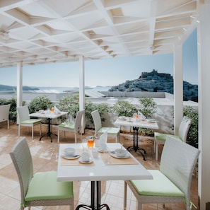 A terrace with tables and chairs, overlooking a coastal town and sea.