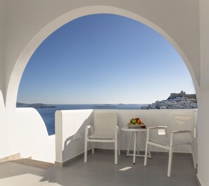 A balcony with two white chairs and a table with a fruit bowl.