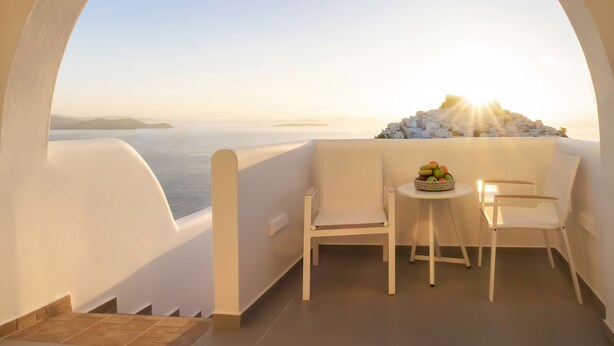 Un balcón con vistas a un pueblo costero, una mesa con fruta y dos sillas.