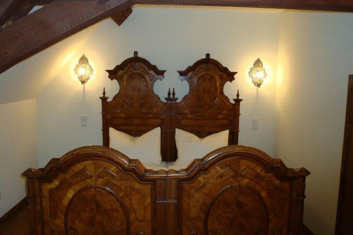 A bedroom with a wooden bed frame, two wall-mounted lamps, and a sloped ceiling.