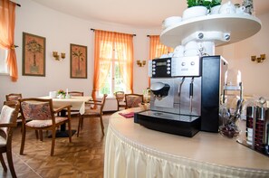 Et spiseområde med kaffemaskine, stole, et bord og et vindue med gardiner.