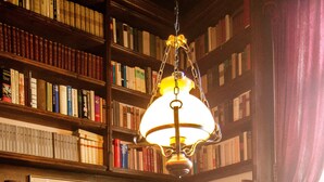 Una biblioteca con estanterías, una mesa redonda con lámpara y un sofá.