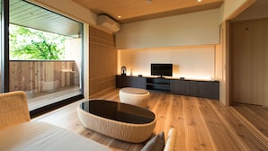 A modern living room with a large window, a flat-screen TV, and a wicker coffee table. - Hotel Hakuba Hifumi (Hakuba)
