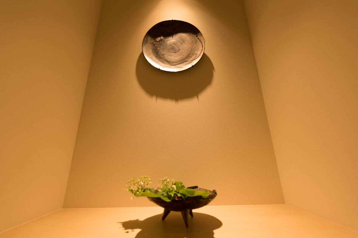 Une pièce au décor minimaliste, avec une seule table, un récipient fixé au mur et une plante en pot.