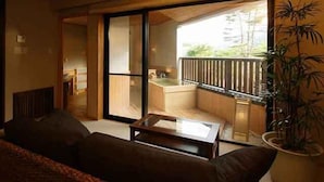 A modern living room with a sofa, a coffee table, and a sliding glass door leading to a balcony with a view of a building and a pool. - Hotel Hakuba Hifumi (Hakuba)